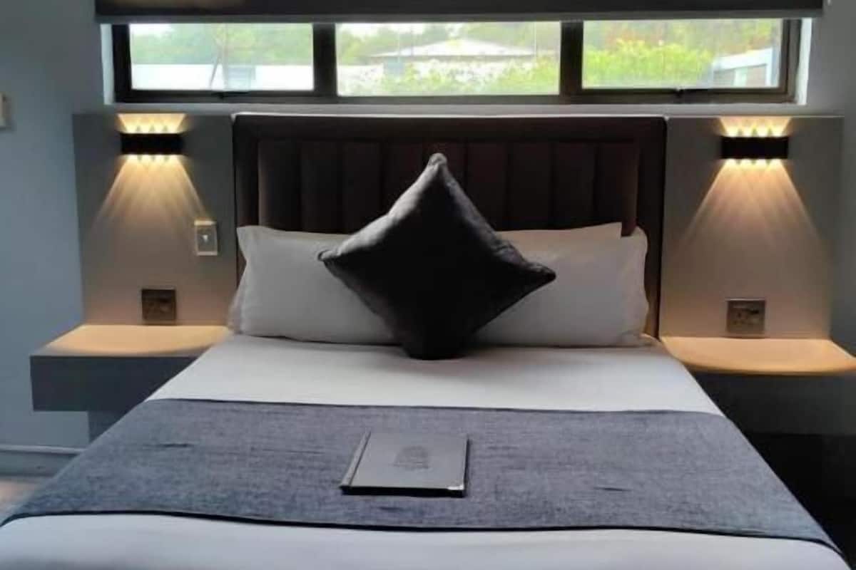 Un dormitorio moderno con una cama grande, dos lámparas de noche, una ventana con vistas y un cabecero oscuro.