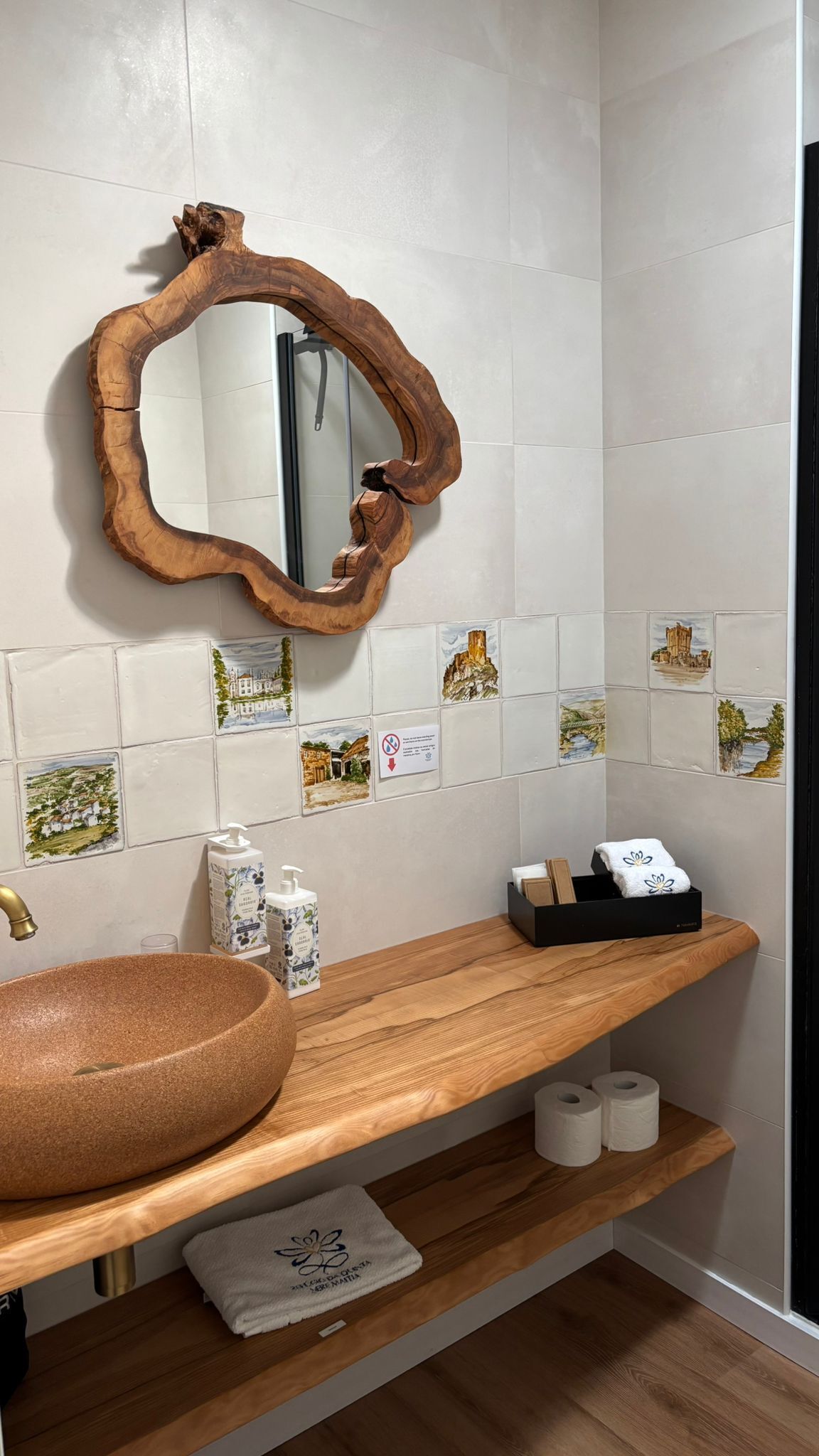 Un baño con tocador de madera, un lavabo redondo, un espejo de marco original y baldosas decorativas en la pared.