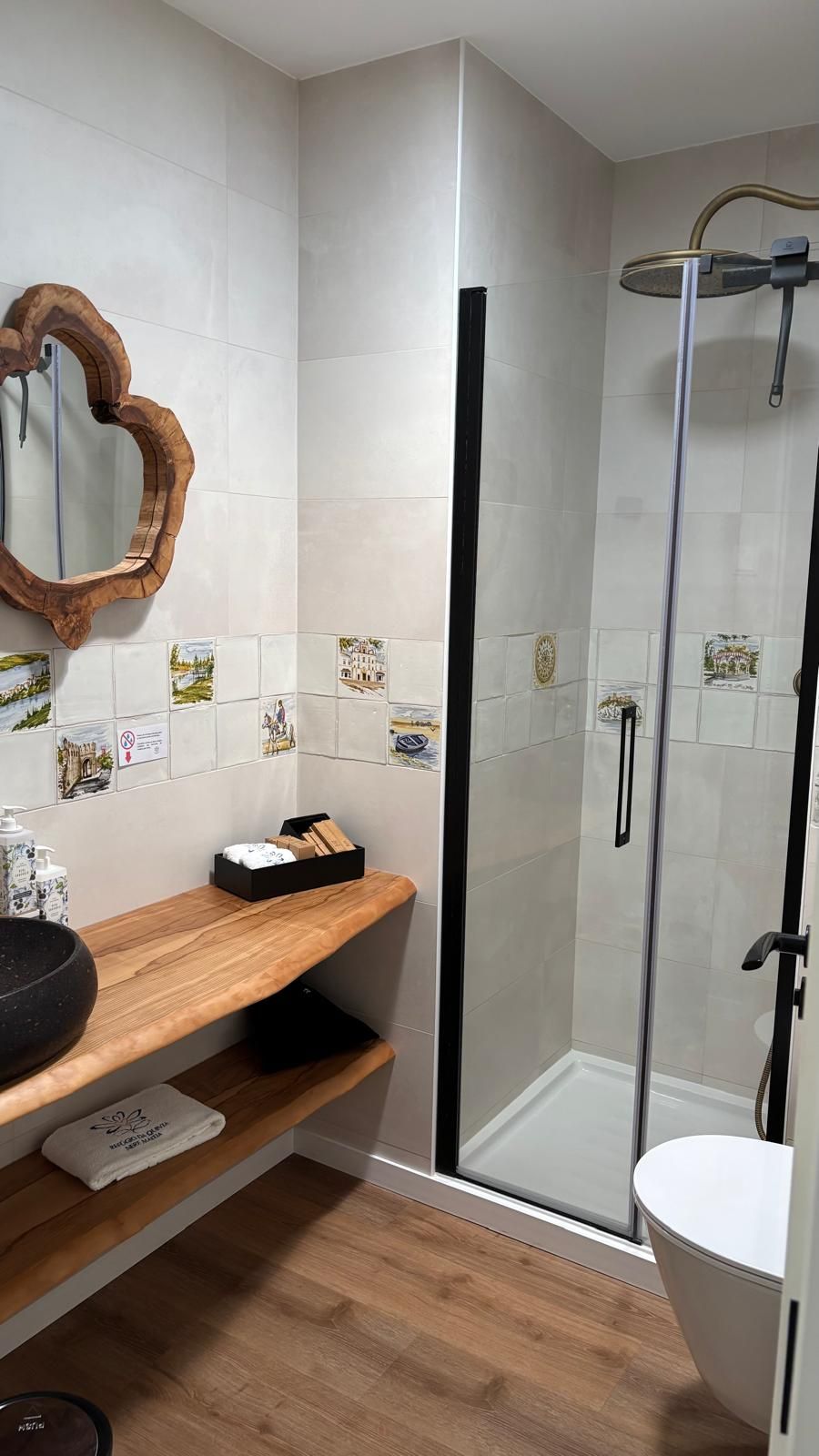 Un baño moderno con tocador de madera, cabina de ducha con mampara de vidrio y azulejos decorativos en las paredes.