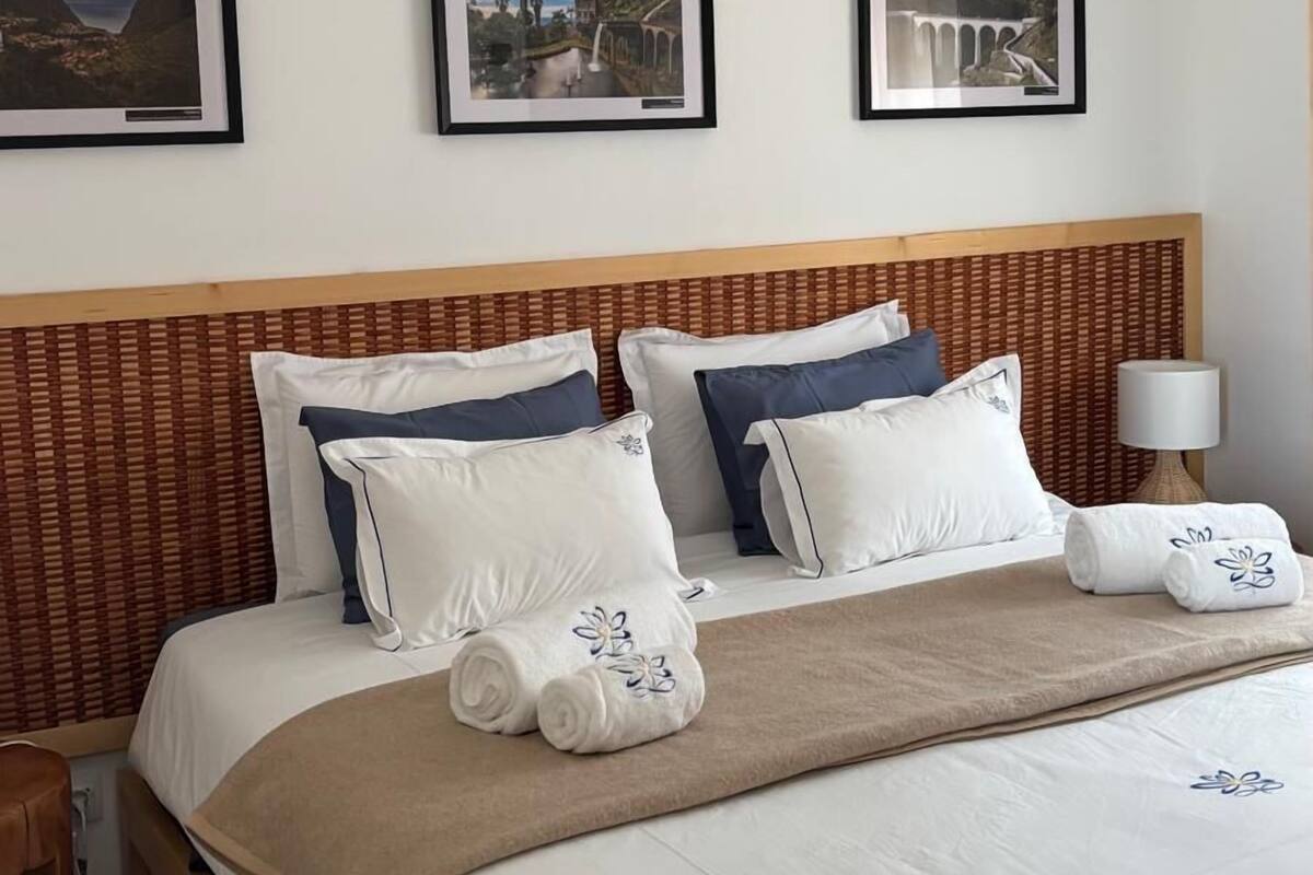A hotel room with a bed, pillows, a headboard, a lamp, and three framed pictures on the wall.