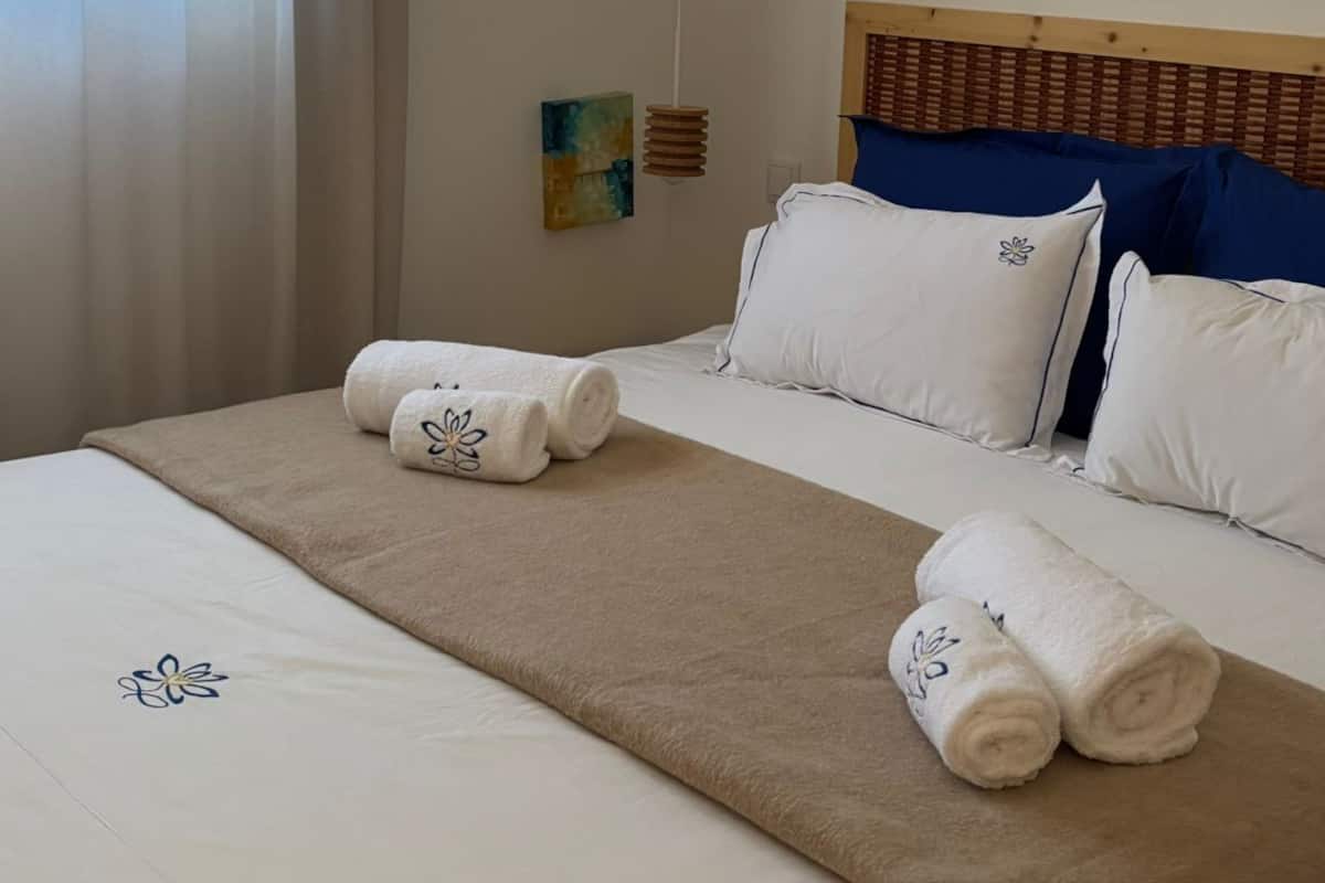 A neatly made bed with white and beige bedding, a wooden headboard, and a small wall art piece.