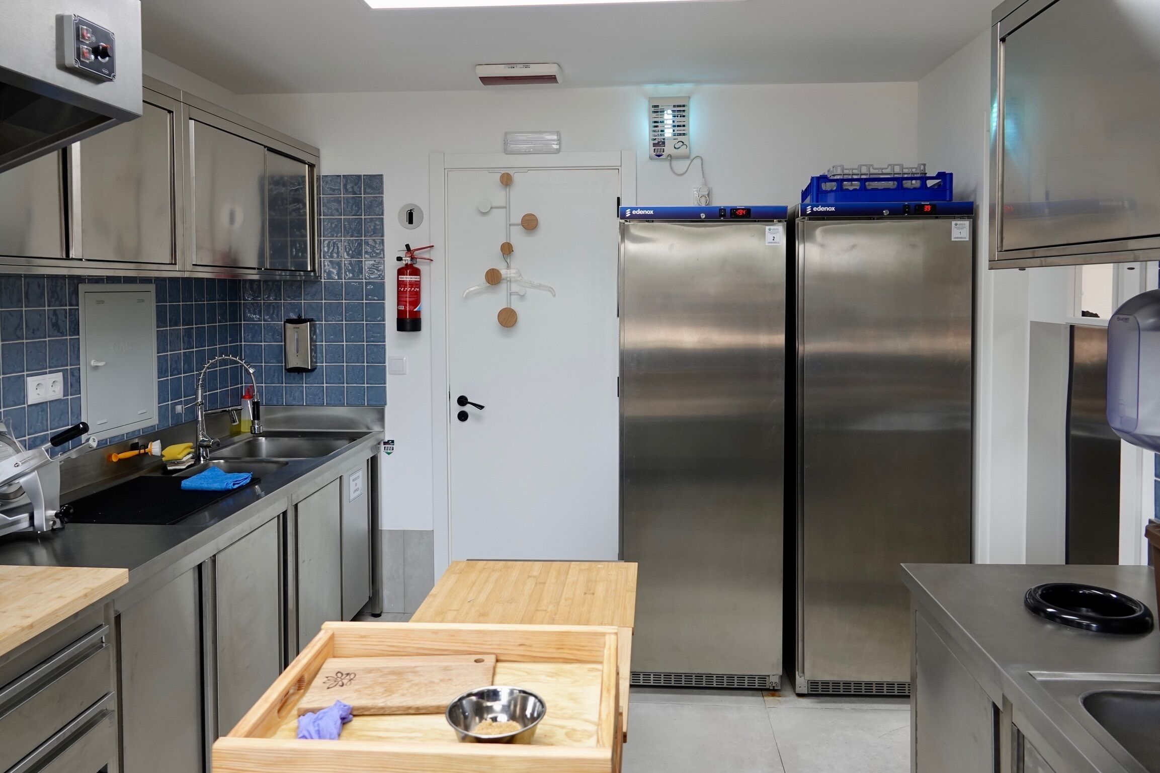 Cocina compacta con electrodomésticos de acero inoxidable, una mesa de madera y un salpicadero de azulejos azules.