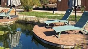 A pool area with lounge chairs and umbrellas, surrounded by trees and a wooden deck. - Refúgio da Quinta Nere Maitia (Santarem)