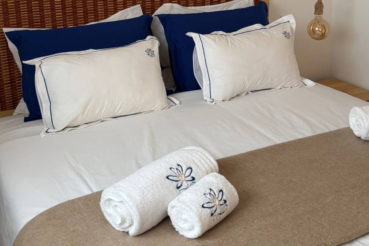 A hotel room with a large bed, two framed pictures on the wall, a hanging light fixture, and two towels on the bed.