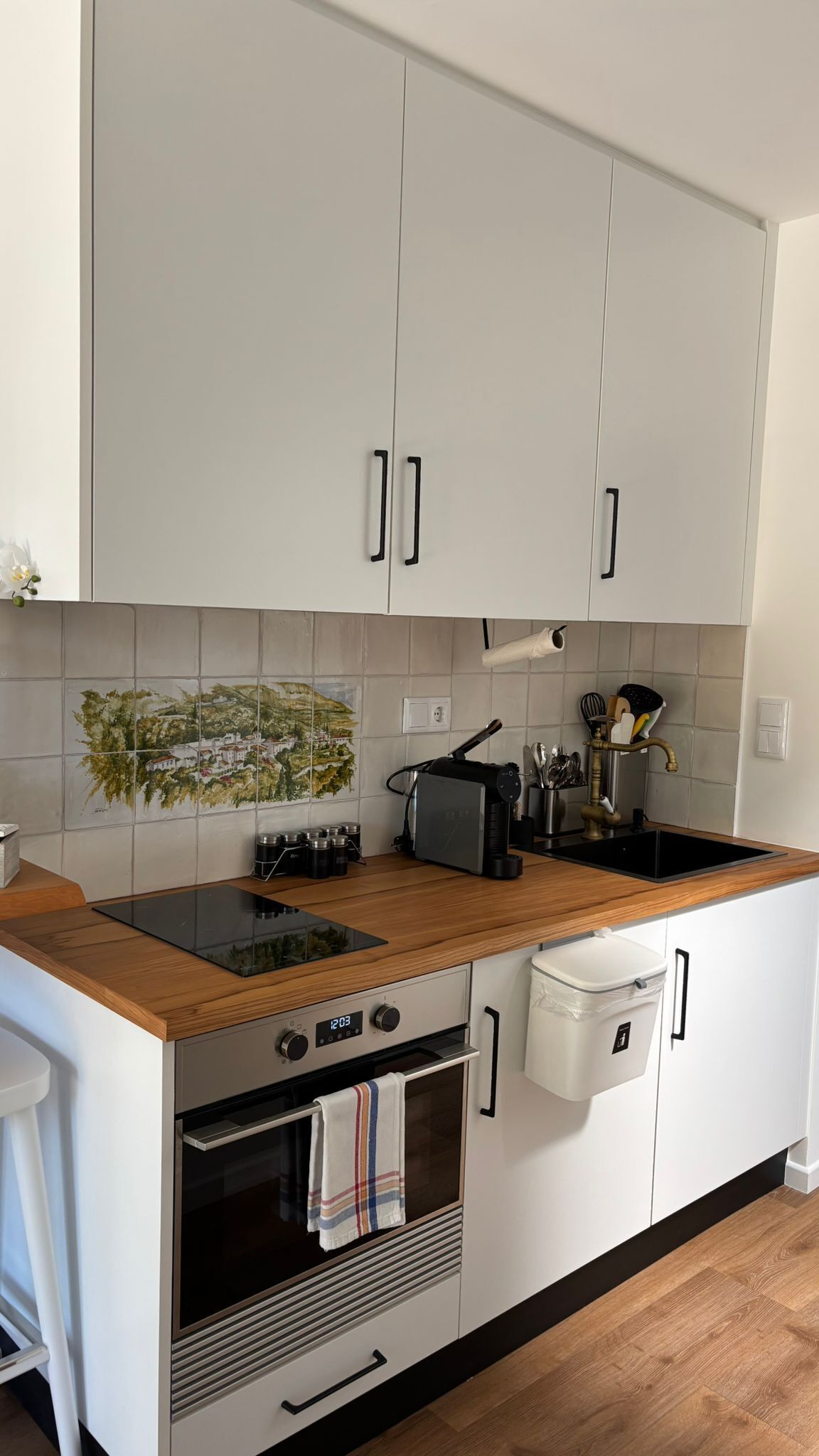 Eine moderne Küche mit weißen Schränken, einer Holz Arbeitsplatte, einem eingebauten Backofen und einer Spritzschutzleiste mit einem Stadtbild-Fliesenmuster.