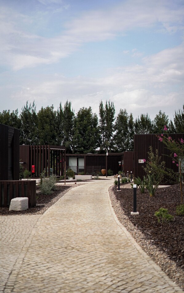 Un chemin pavé mène à un bâtiment à la façade en bois sombre, entouré de verdure et d’arbres.