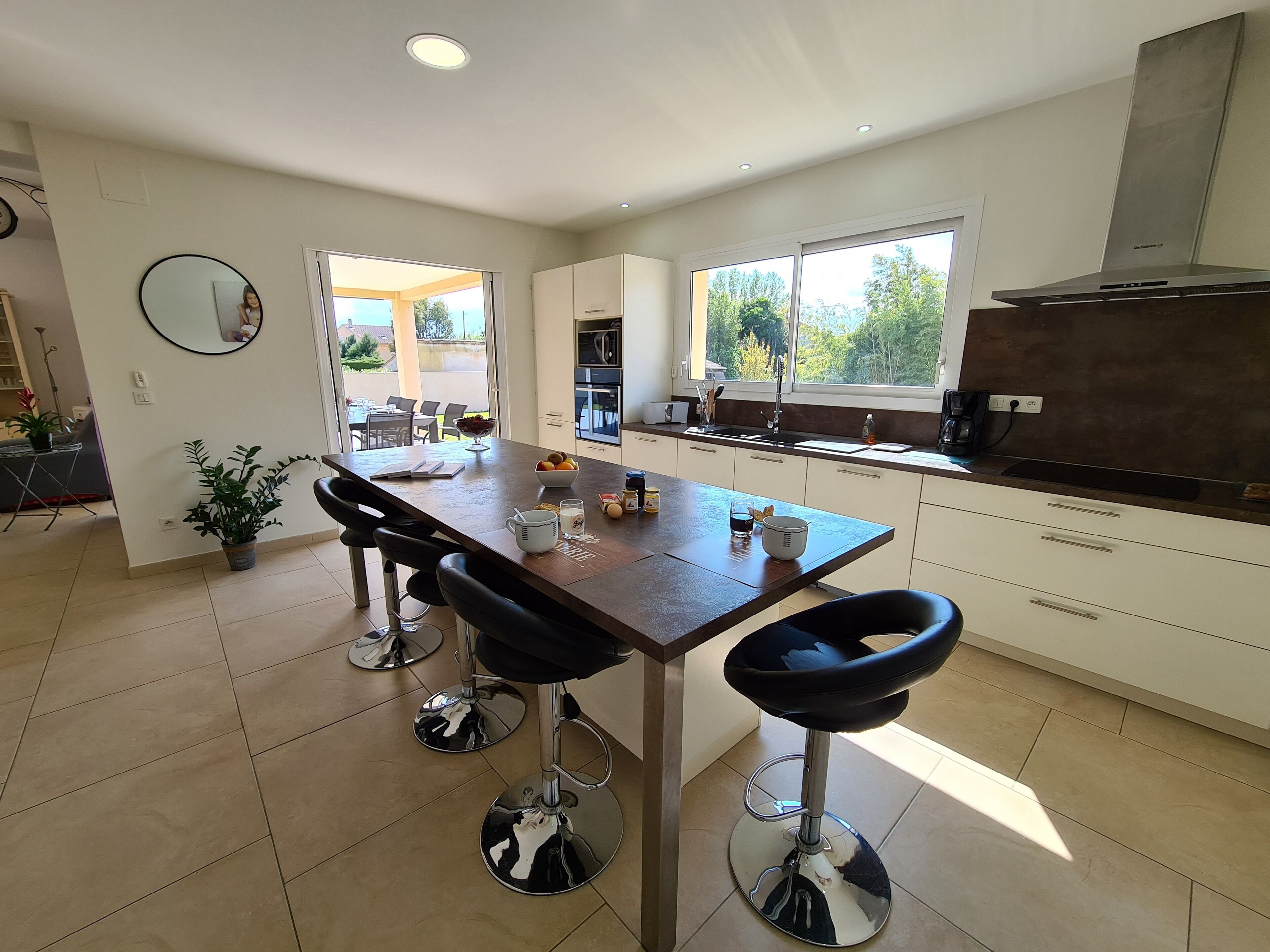 A modern kitchen with a central island, bar stools, a large window, and a view of the outdoors.