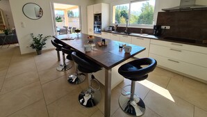 A modern kitchen with a central island, bar stools, a large window, and a view of the outdoors.