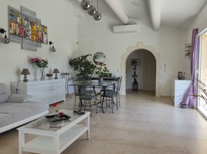 Un salón moderno con sofá, mesa de centro, mesa de comedor y sillas. Hay un cuadro en la pared, una planta en maceta y una lámpara.