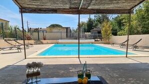 A pool area with lounge chairs, a table with drinks, and a pergola.