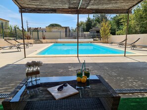 Zona de piscina con sillones de descanso, una mesa con bebidas y una pérgola.