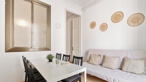 Ein Essbereich mit einem weißen Tisch und schwarzen Stühlen, eine weiße Couch mit beigen Kissen sowie drei gewebte Wanddekorationen.