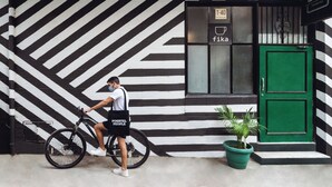 Uma pessoa de bicicleta em frente a um edifício com fachada listrada em preto e branco e porta verde.