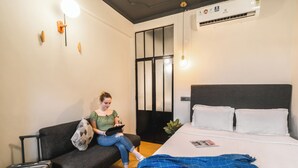 Quarto de hotel moderno com cama, sofá, mesa pequena e mala.