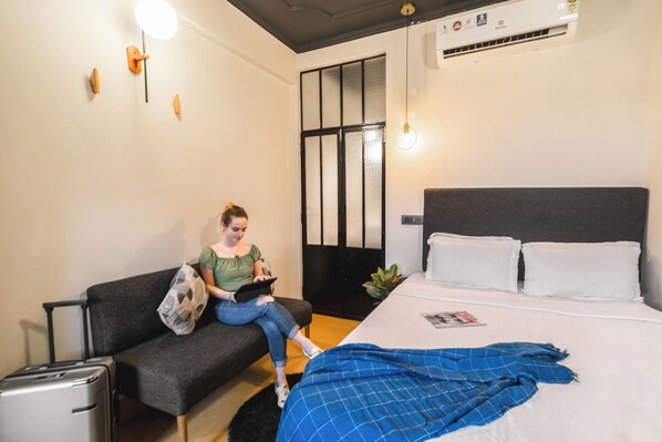 A modern hotel room with a bed, a sofa, a small table, and a suitcase. - Minimalist One Hauz Khas VIllage (New Delhi)