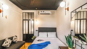 Quarto de hotel com uma cama, um sofá, uma planta em vaso e ar condicionado fixado na parede.