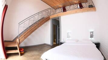 Un dormitorio con una cama grande, una escalera de madera y un escritorio pequeño.