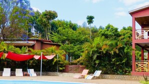 Una piscina con sillones de descanso y un toldo rojo.