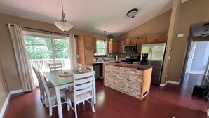 A modern kitchen with wooden cabinets, a central island, stainless steel appliances, and a dining area with a table and chairs. - NEW Spacious Home Minutes From Oneida Lake & Fall Festivities!  (Brewerton)