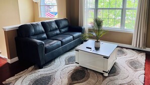 A living room with a black leather sofa, a white coffee table, and a potted plant. - NEW Spacious Home Minutes From Oneida Lake & Fall Festivities!  (Brewerton)