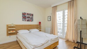 A double bed with a wooden headboard, a bedside table with a lamp, a framed picture on the wall, and a window with curtains. - ShortStayPoland Wileńska B165 (Warsaw)