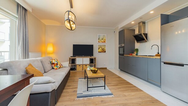 A modern apartment with a living room, kitchen, and dining area. It features a sofa, a coffee table, a TV, and a refrigerator. - ShortStayPoland Wileńska B165 (Warsaw)