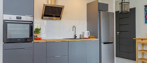 A modern kitchen with grey cabinets, a built-in oven, a stainless steel refrigerator, and a microwave.