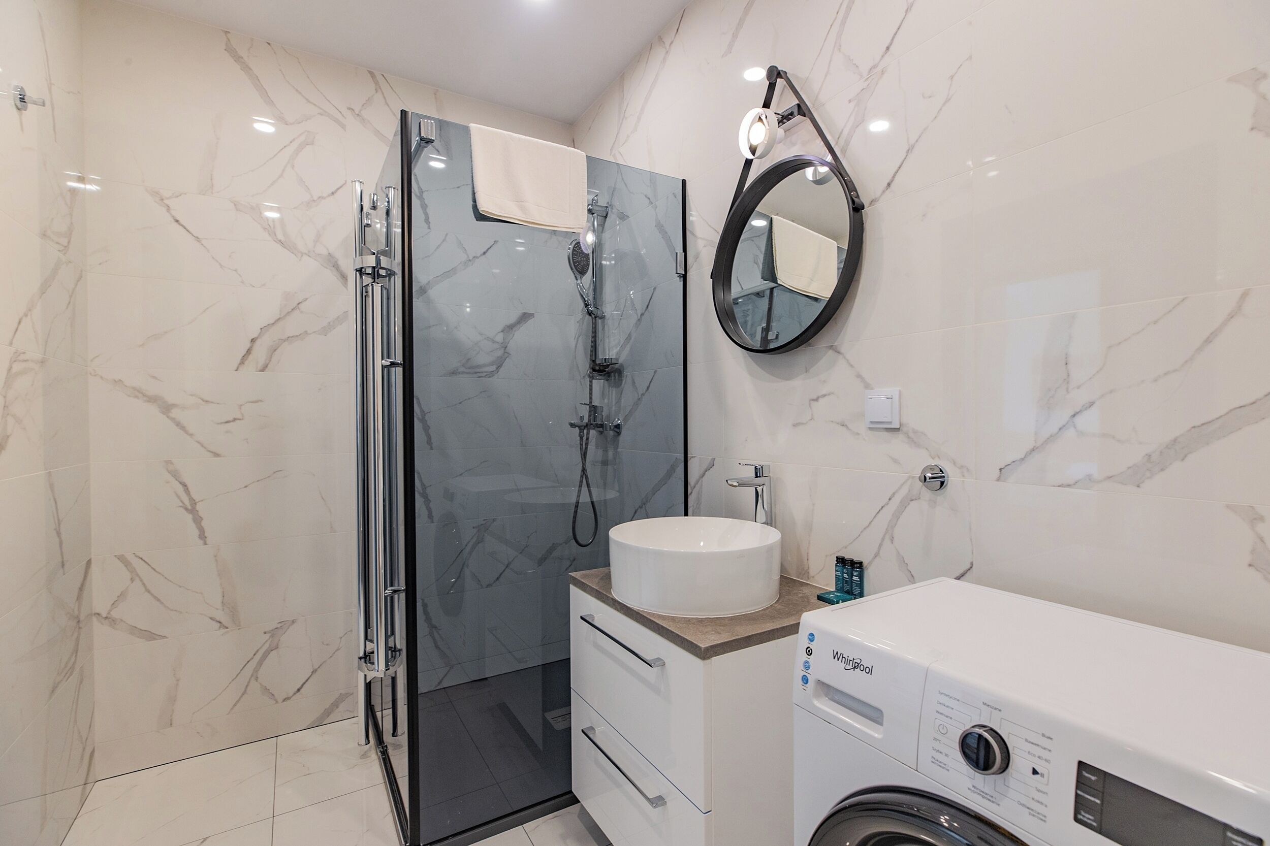 A modern bathroom with a glass-enclosed shower, a white sink, and a built-in washing machine.