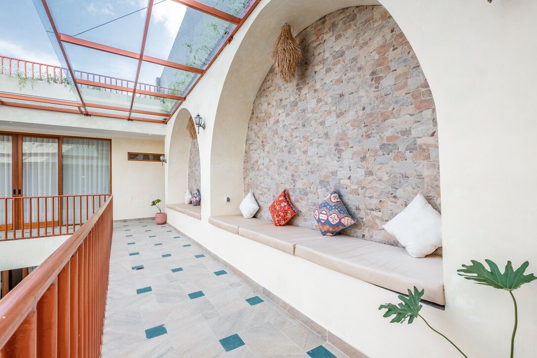 A spacious balcony with a glass roof, stone walls, and a seating area with cushions.