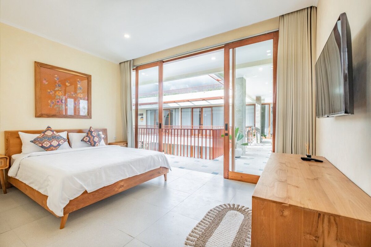 A bedroom with a bed, a wooden desk, a TV, and a balcony with a railing.