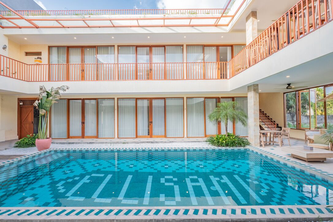 A modern hotel with a central swimming pool, a second-floor balcony, and a staircase leading to the upper level.