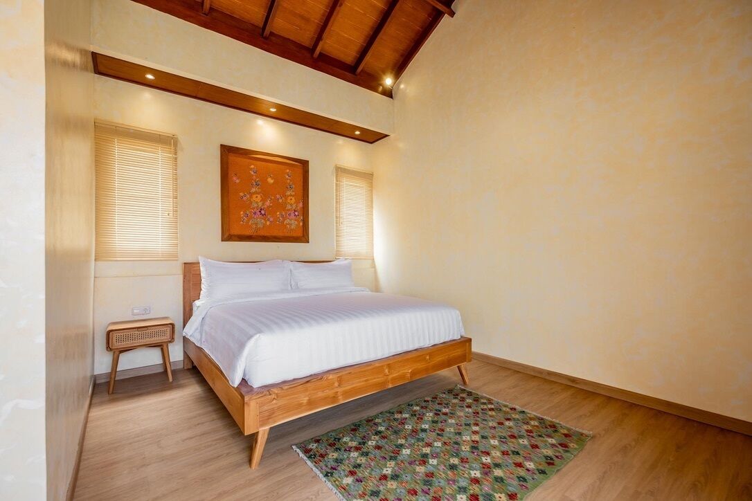 A bedroom with a wooden bed, a small bedside table, a wall-mounted painting, and a patterned rug.
