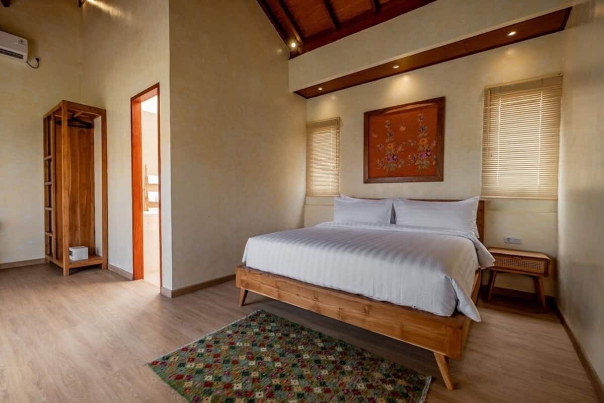 Un dormitorio con cama de madera, un tapete colorido, un armario de madera y un cuadro en la pared.