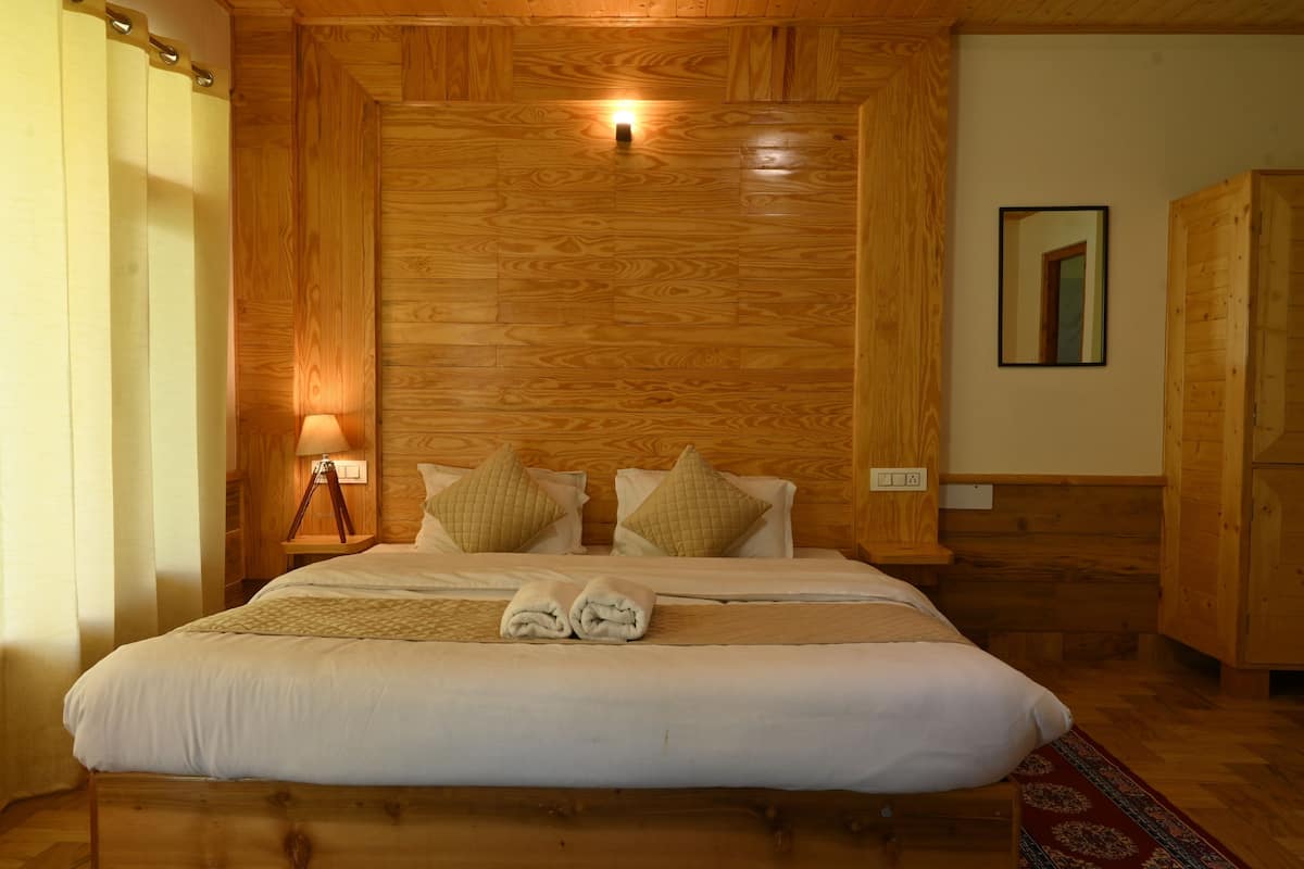 Un dormitorio con paneles de madera, una cama, almohadas, una lámpara de noche y un espejo en la pared.
