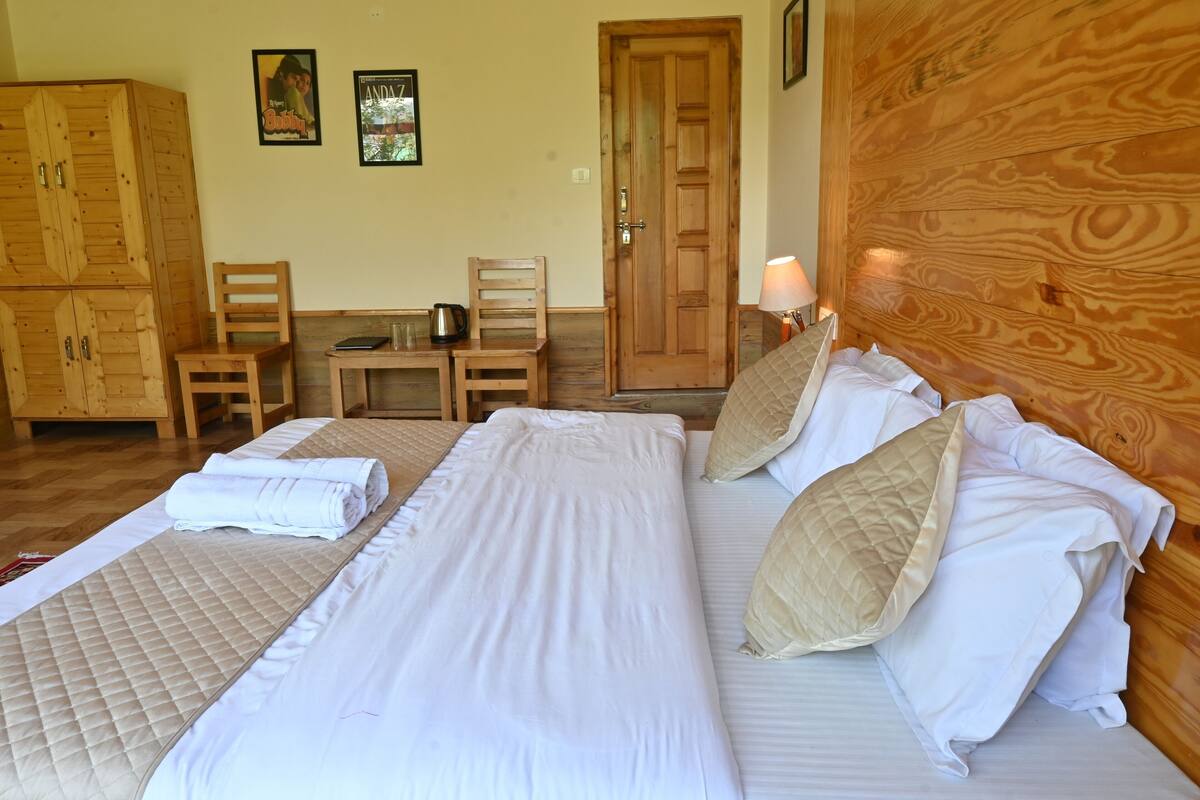 Un dormitorio ordenado con cama, dos sillas, una mesita y un armario de madera.