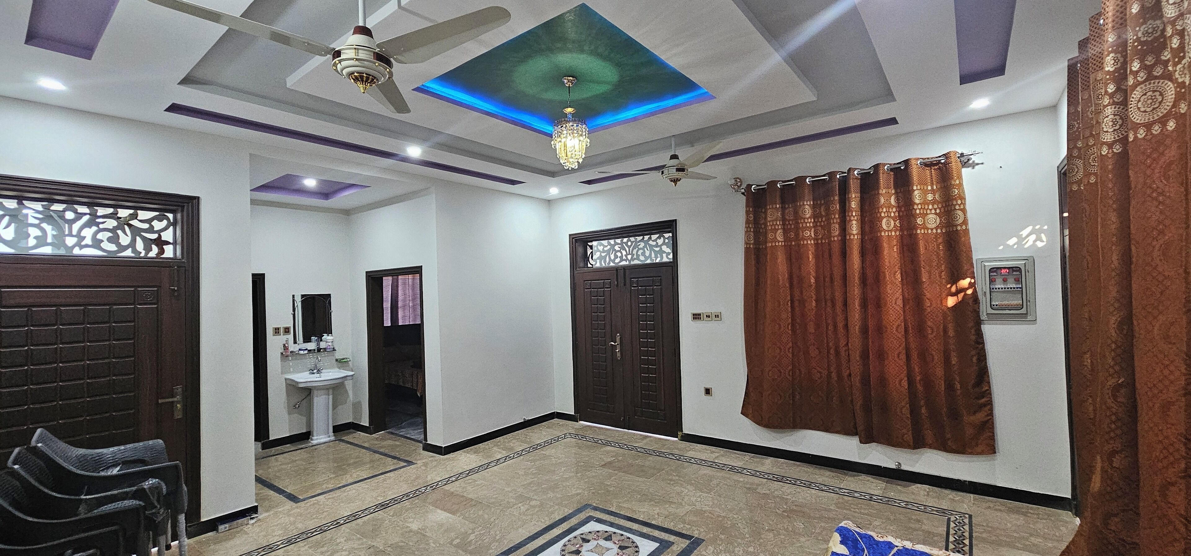 Un intérieur moderne agrémenté d’un ventilateur de plafond, d’un lustre, de rideaux à motifs et d’un sol carrelé.