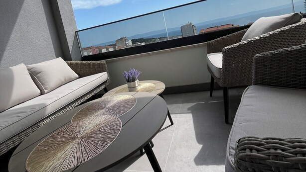 A balcony with a sofa, a small table, and a wicker chair. - Apartment Ema (Makarska)