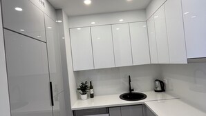 A modern kitchen with white cabinets, a black sink, and a built-in oven. - Apartment Ema (Makarska)