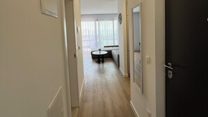A hallway with a dark door on the right, a round table with a vase in the center, and a sofa in the background. - Apartment Ema (Makarska)