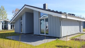 Una casa moderna con un'ampia porta-finestra in vetro, un portico coperto e un prato curato.