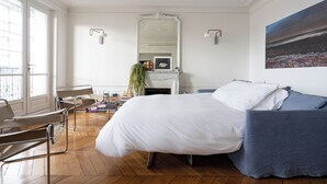 A bedroom with a large bed, a blue sofa, a chair, a fireplace, and a large window. - 2 BD lovely APT facing Canal St Martin sleeps 6! (Paris)