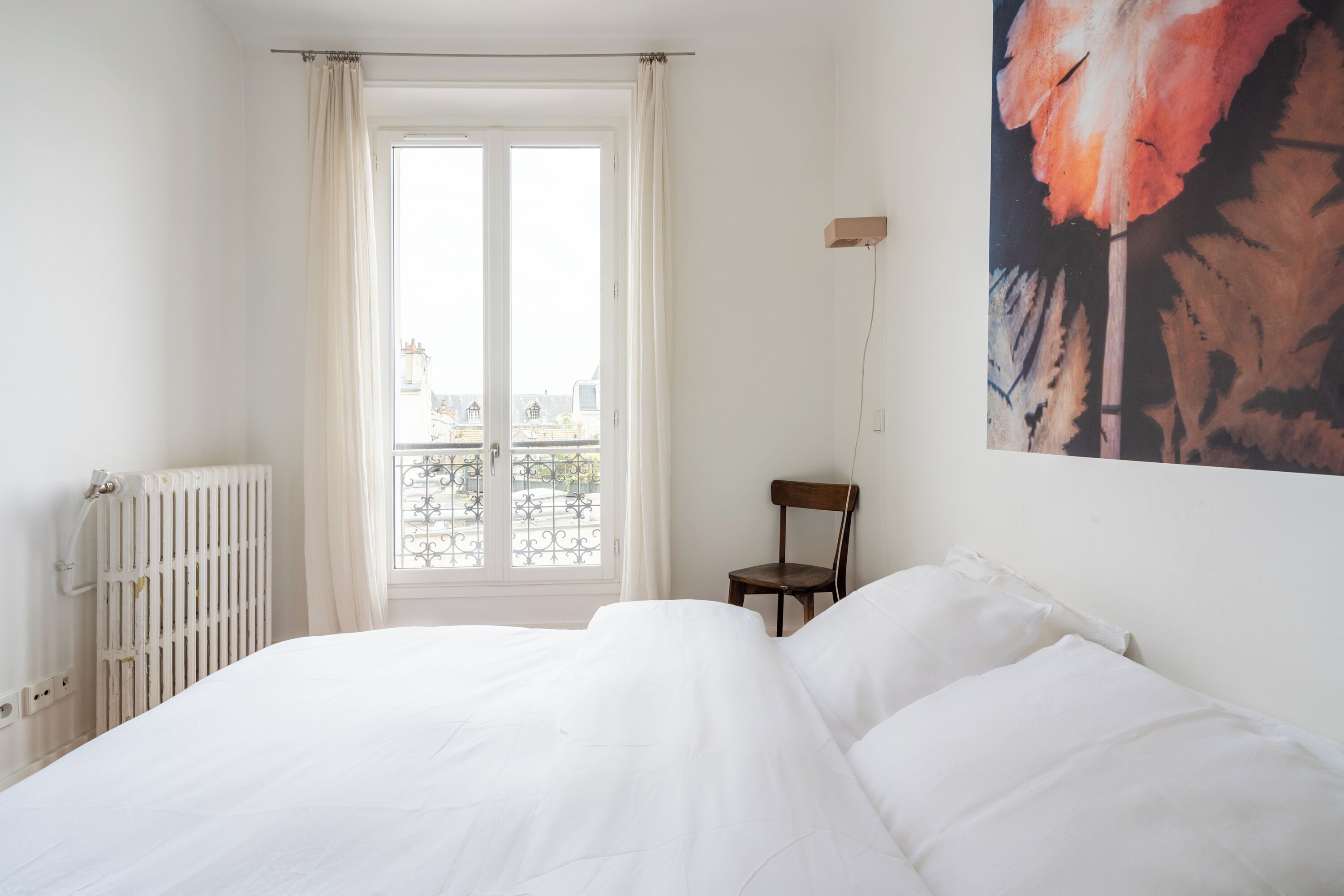 A bedroom with a large bed, a chair, a radiator, and a window with curtains.