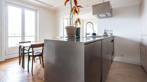 A modern kitchen with a central island, a dining area with chairs, and a large window providing natural light. - 2 BD lovely APT facing Canal St Martin sleeps 6! (Paris)