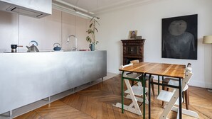 A modern kitchen with a central island, a dining table with chairs, and a large abstract painting on the wall. - 2 BD lovely APT facing Canal St Martin sleeps 6! (Paris)