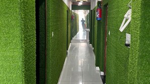 A hallway with green artificial grass walls, a tiled floor, and a ceiling with recessed lighting and a smoke detector. - Hotel Neki & Restaurant (Meerut)