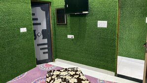 A room with green artificial grass walls, a flat-screen TV mounted on the wall, a door with a geometric pattern, and a patterned rug on the floor. - Hotel Neki & Restaurant (Meerut)