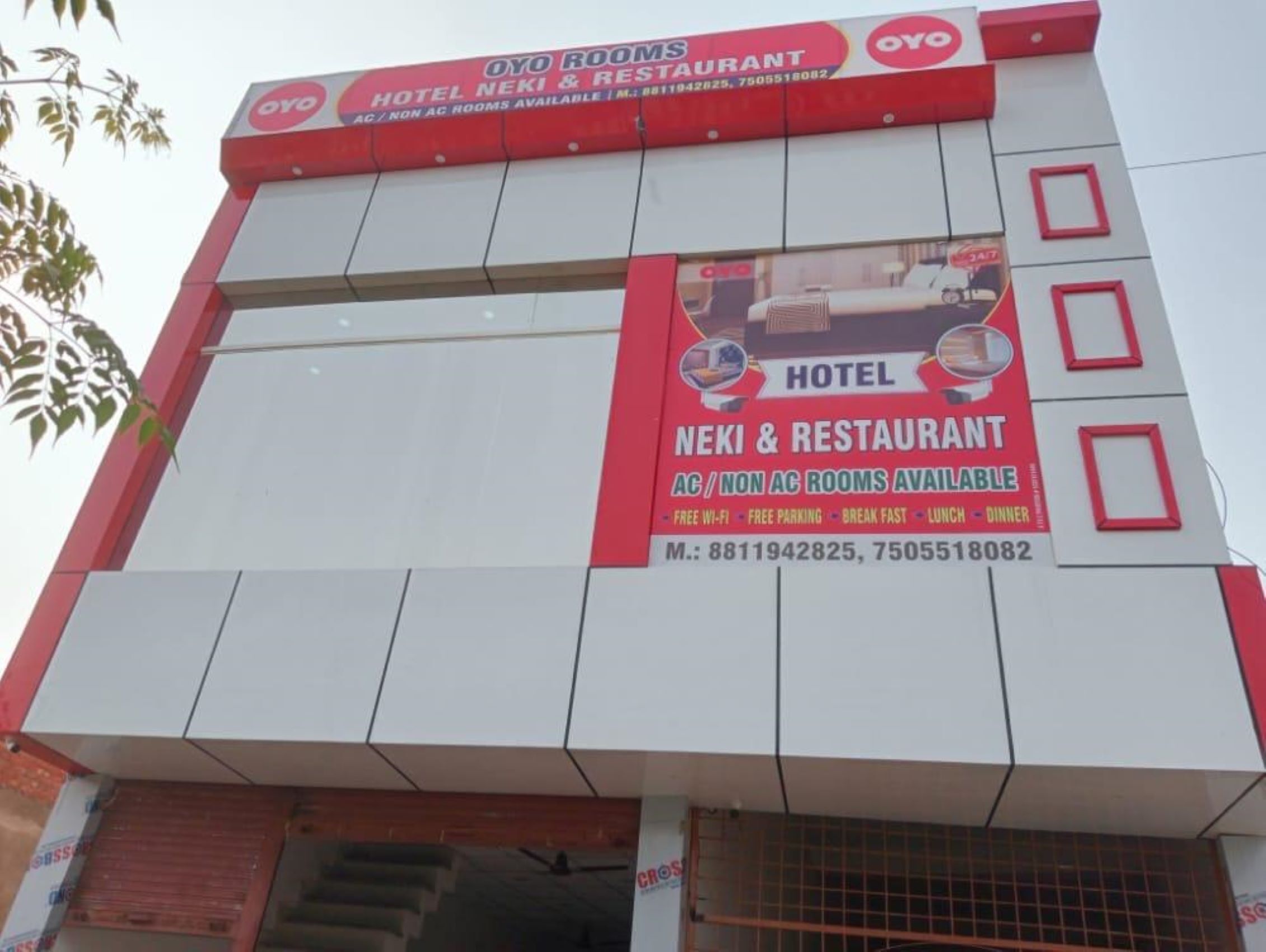 A hotel with a red and white facade, featuring a prominent sign advertising AC and non-AC rooms, free Wi-Fi, and a restaurant.