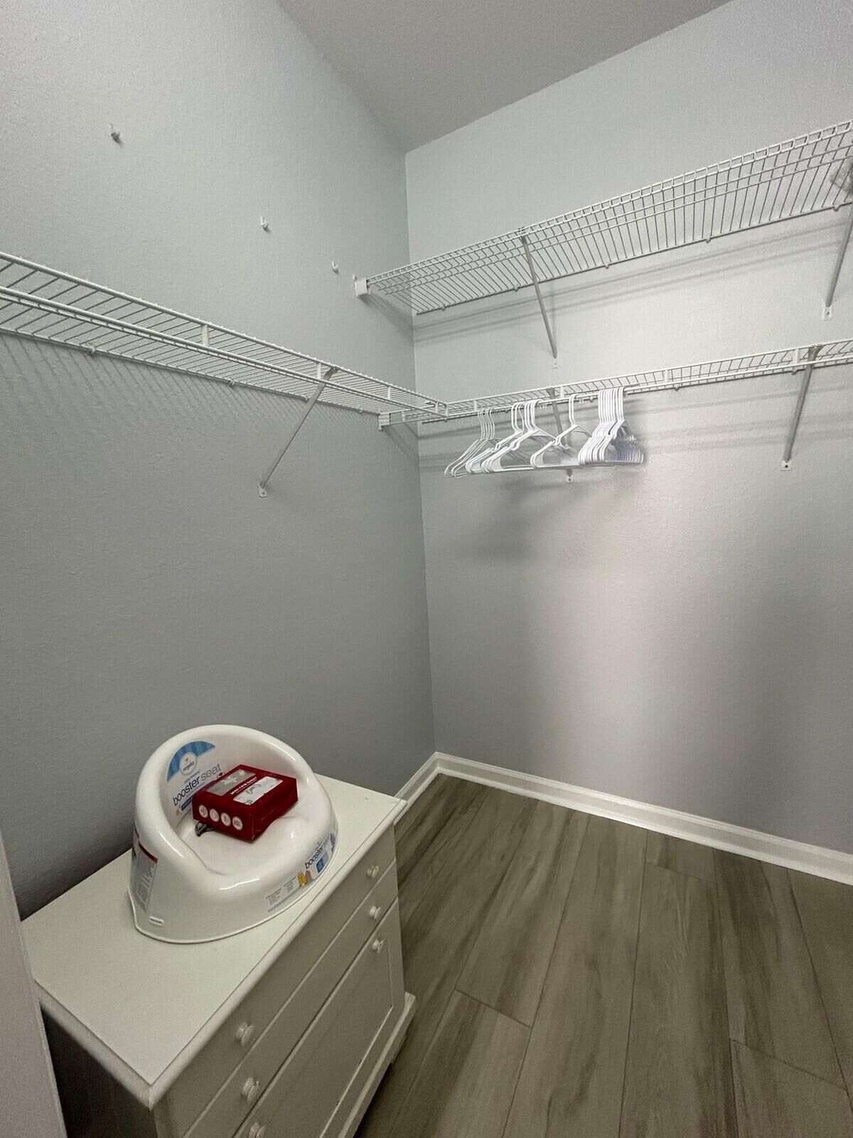 Una habitación pequeña y estrecha con paredes grises y suelo de madera. Tiene un aparador blanco, una lavadora blanca y dos tendederos metálicos en las paredes.