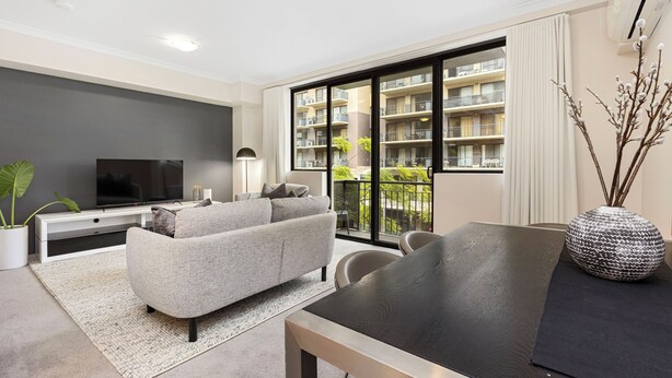 A modern living room with a grey sofa, a flat-screen TV, a dining table, and a large window with a view of a building. - Executive Elegance: Stylish 1BR Suite on Hay St (East Perth)