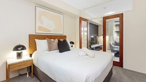 A hotel room with a large bed, a nightstand with a lamp, a painting on the wall, and a door leading to a balcony. - Executive Elegance: Stylish 1BR Suite on Hay St (East Perth)